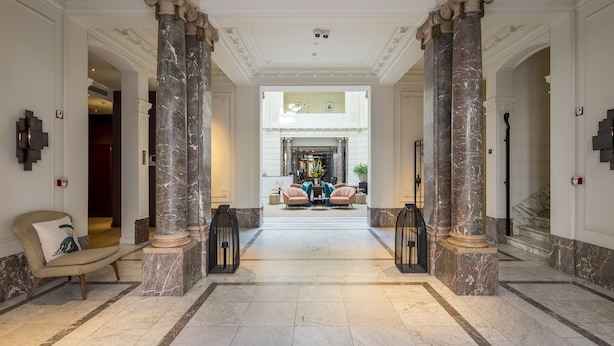 Un lobby imponente con columnas de mármol, una zona de estar central y una escalera que conduce a un nivel superior.