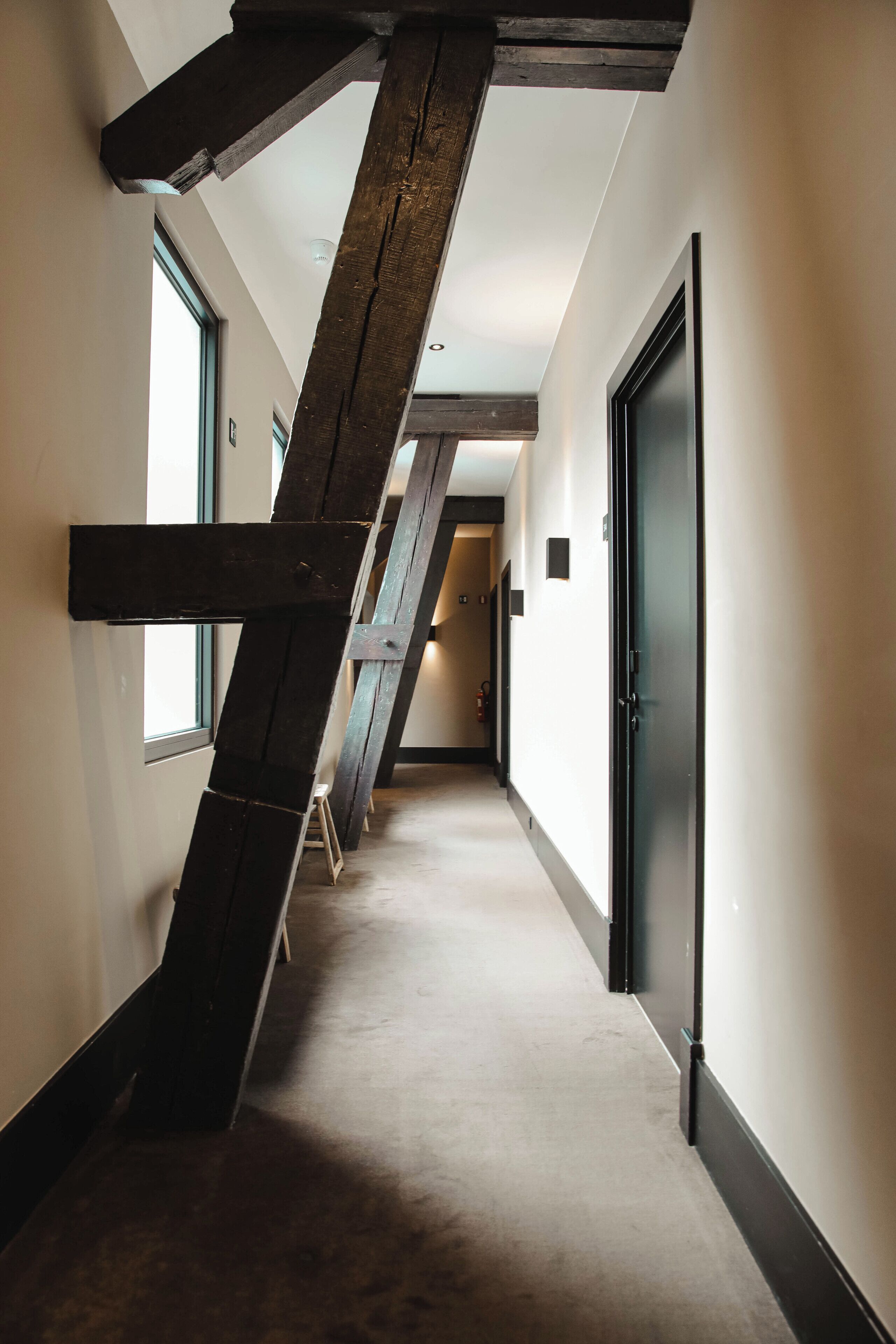 Un couloir étroit avec des poutres en bois apparentes, un sol recouvert de moquette et une porte sur le côté droit.