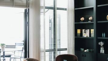 A modern living room with a large window, a black bookshelf, and two leather armchairs.