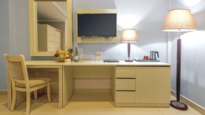 Une chambre d’hôtel avec un bureau en bois, une chaise, une télévision, une lampe et une petite table sur laquelle se trouvent une bouteille et un verre.