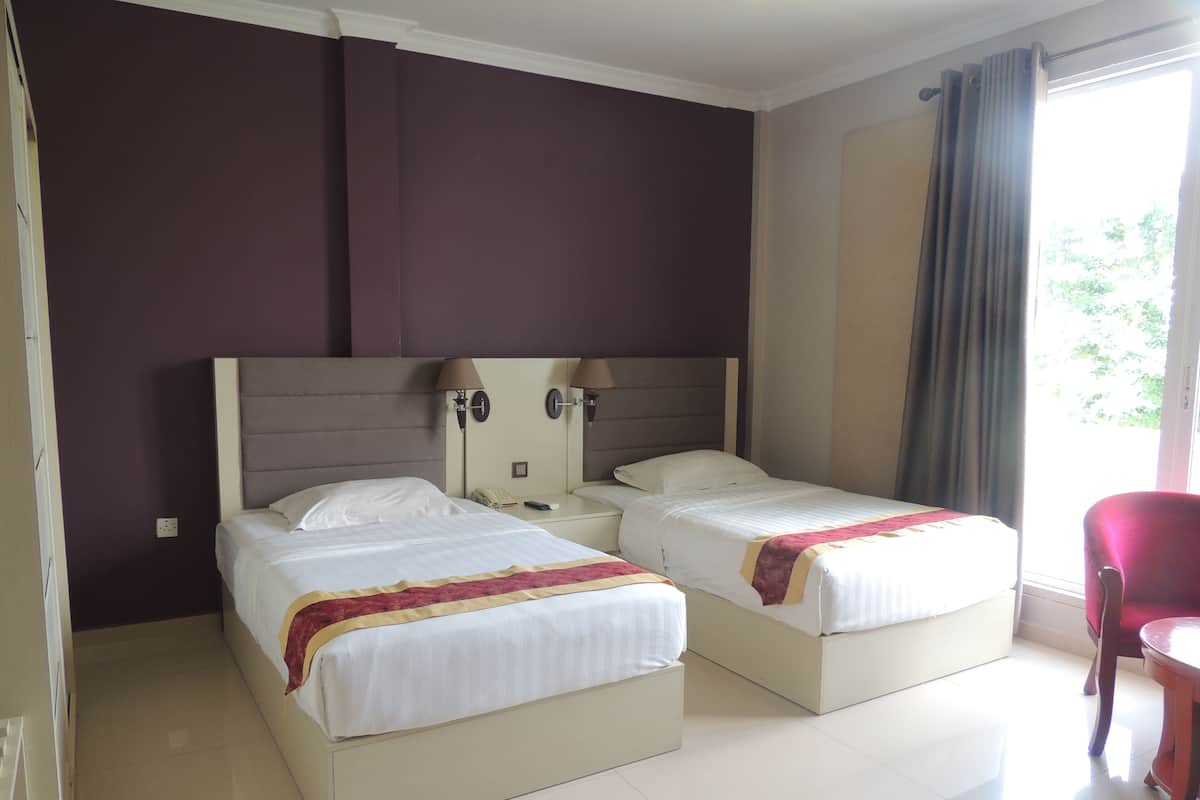 A hotel room with two beds, a nightstand, a red chair, and a window with curtains.