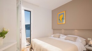 A bedroom with a bed, a nightstand, a painting, and a view of the outdoors. - Villa Lavanda Deluxe (Rogoznica)
