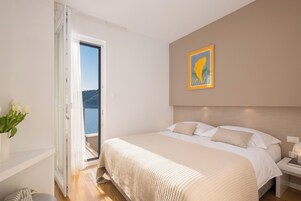 Un dormitorio con cama, mesita de noche, un cuadro y vistas al exterior.