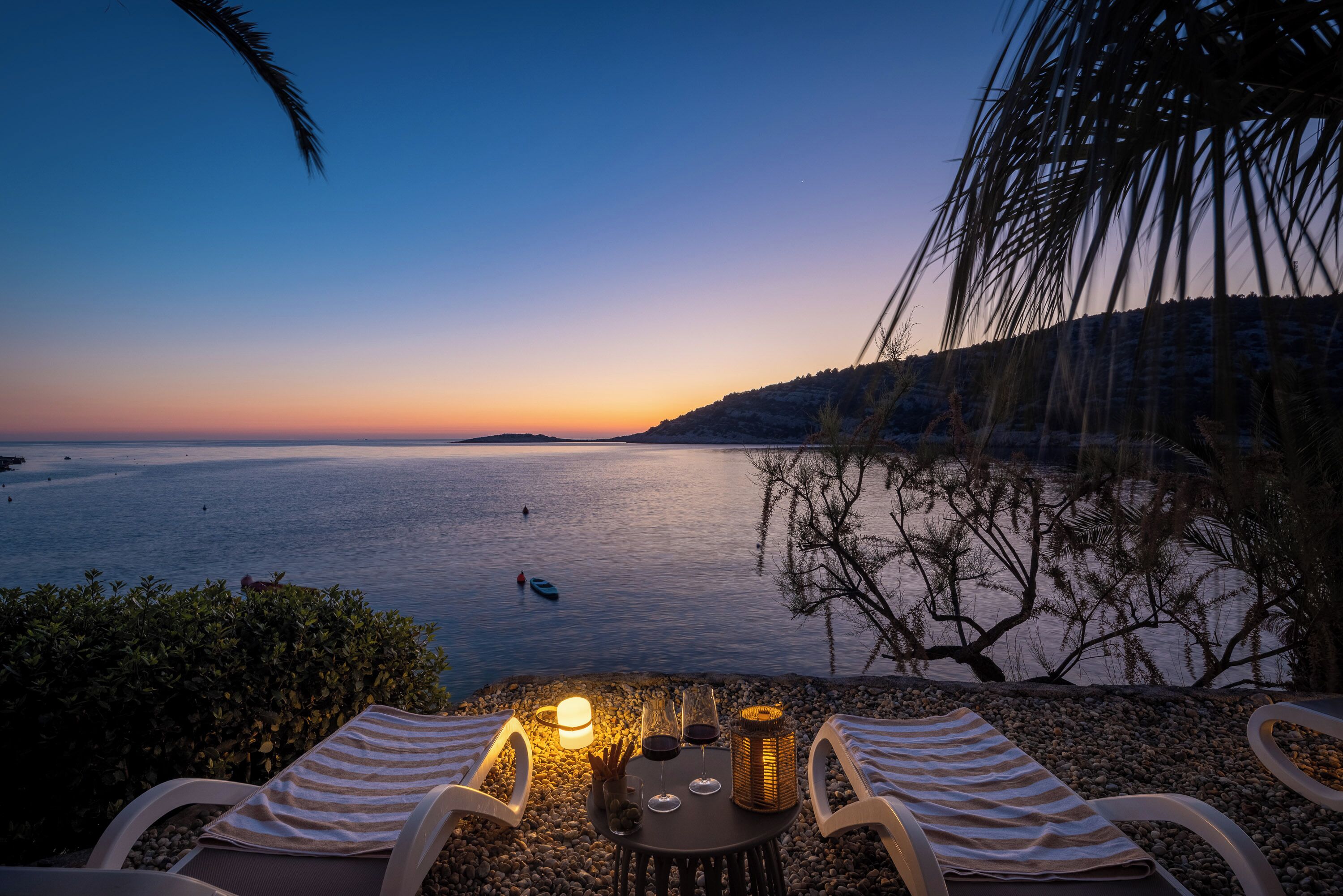 Een zonsondergang uitzicht vanaf een terras met twee loungestoelen, een tafel met drankjes en een kaars.