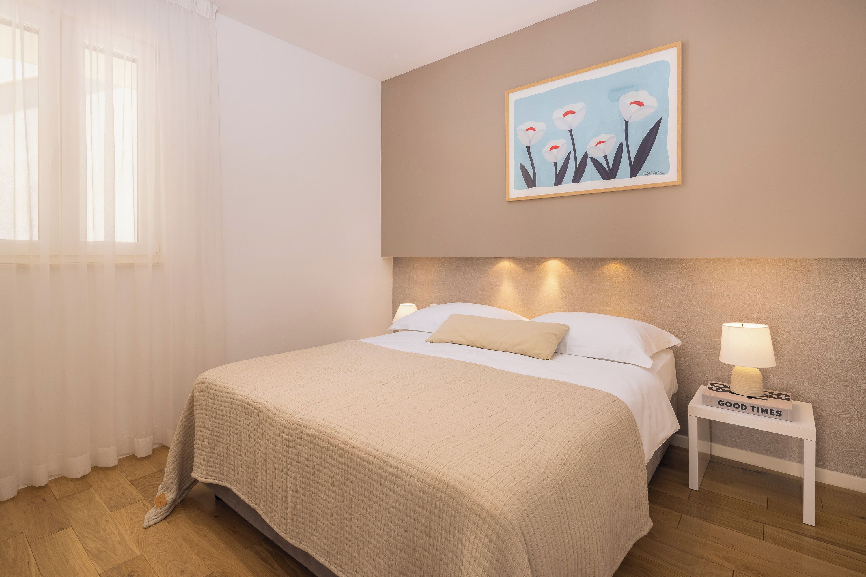 A neatly made bed with a beige blanket, a bedside lamp, and a framed picture on the wall.
