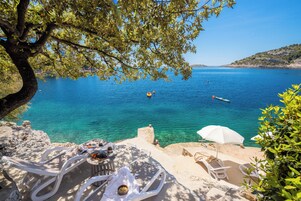 Una terraza frente al mar con mesas al aire libre, una mesa con comida y vistas al océano.