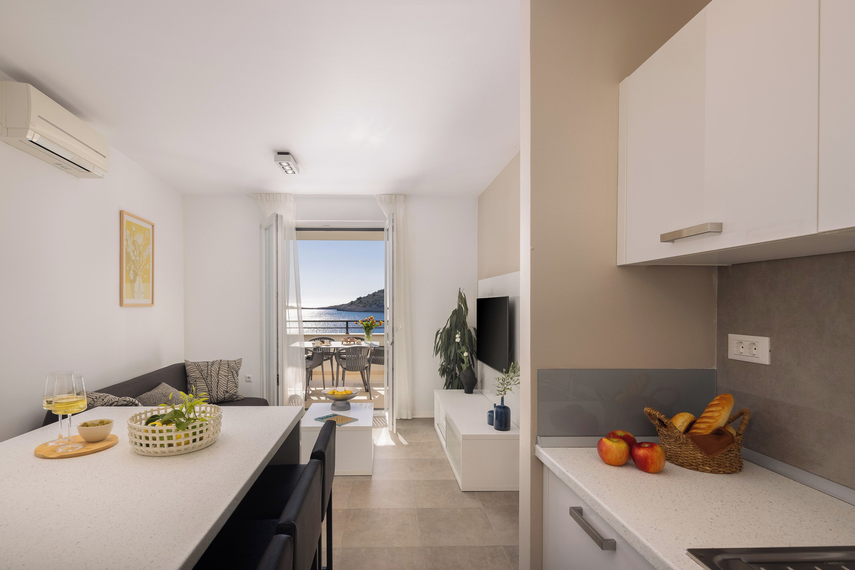 A modern kitchen with a dining area, a TV, and a view of the sea.