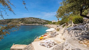 A coastal view with clear blue water, a rocky shoreline, and lounge chairs with umbrellas. - Villa Lavanda Deluxe (Rogoznica)