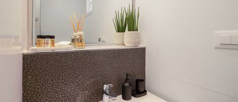 Un baño moderno con un lavamanos blanco, un espejo, una planta en maceta y una pared con textura.