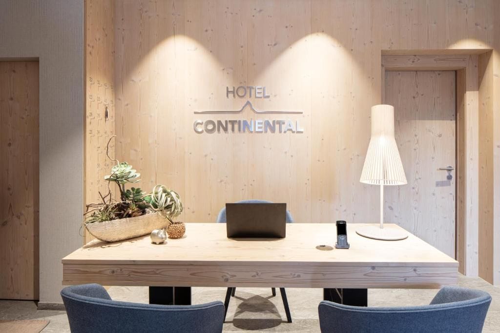 Habitación de hotel con pared de madera, un escritorio con una computadora portátil, un teléfono móvil y una lámpara.
