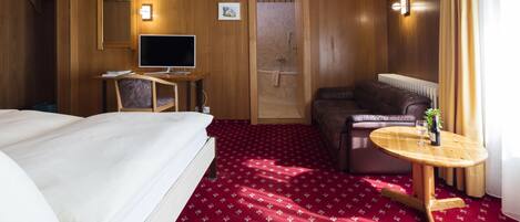 Una habitación de hotel con una cama, un escritorio con computadora, una silla, un sofá y una pequeña mesa con una planta.