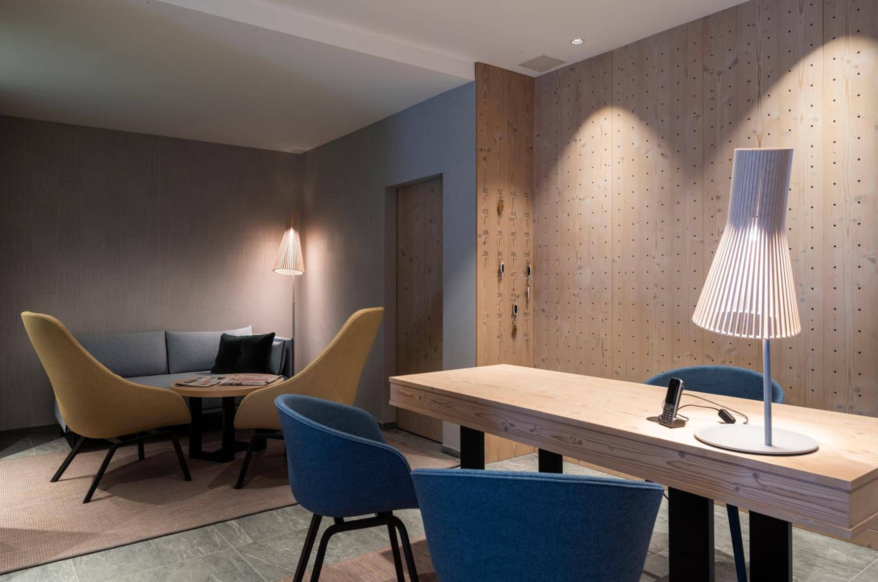 A modern hotel room with a wooden accent wall, a round table with chairs, and a standing lamp.