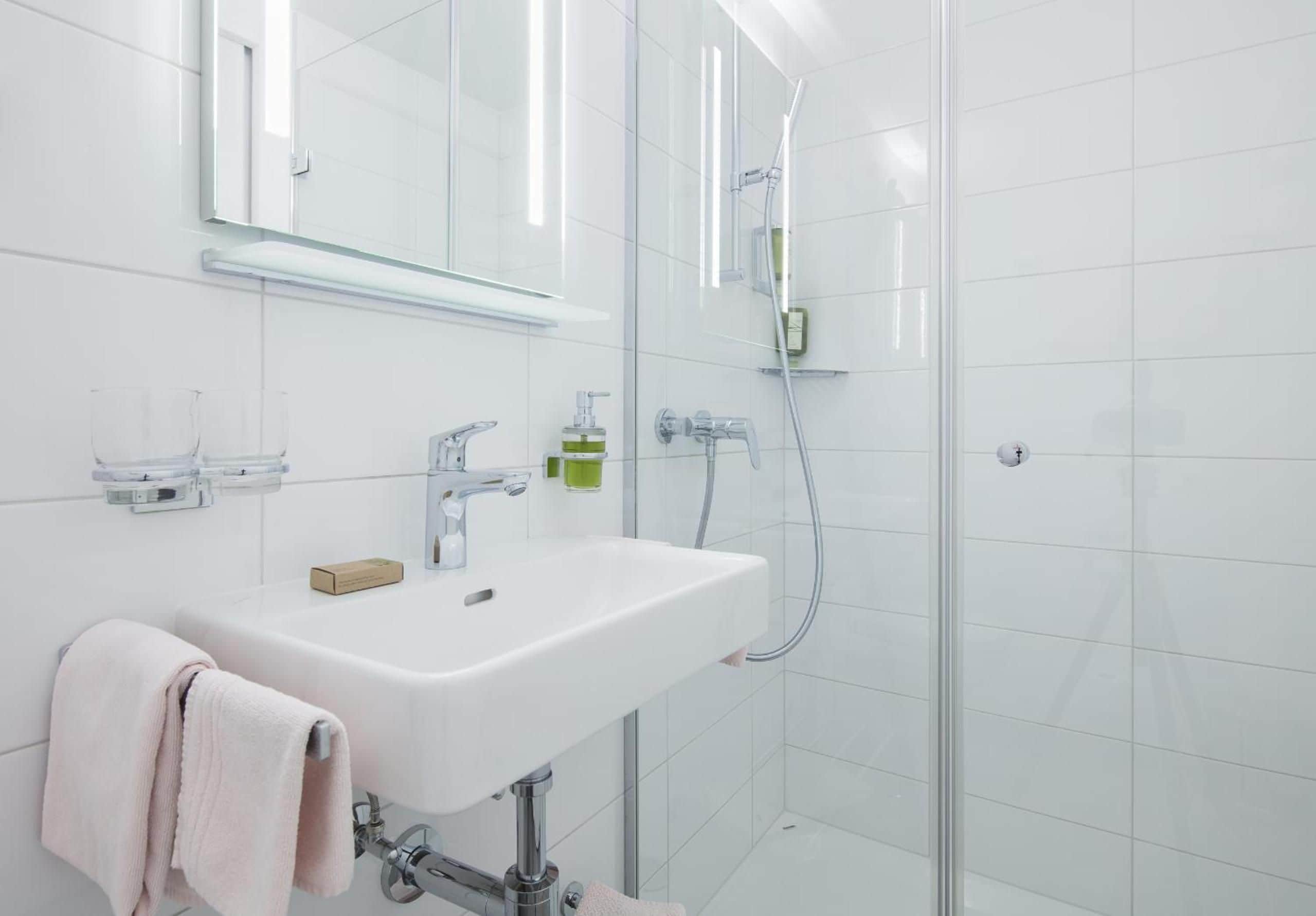 A modern bathroom with a white sink, a mirror, a towel, and a shower area.