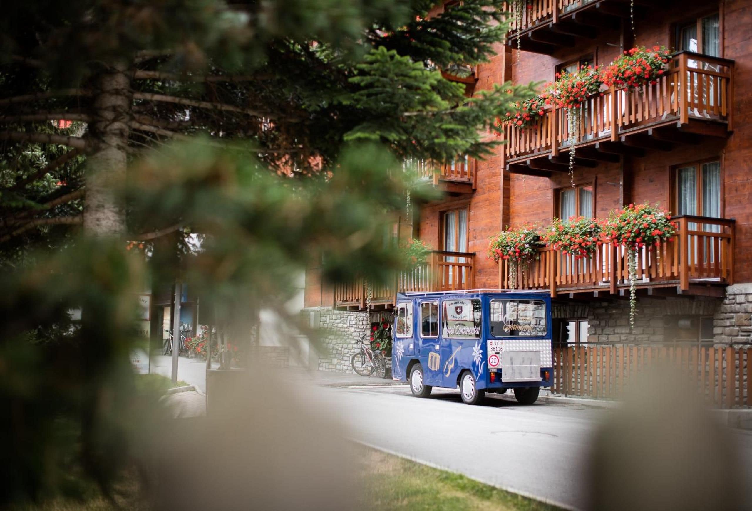 Un camión de comida azul estacionado frente a un edificio con macetas rojas de flores en el balcón.