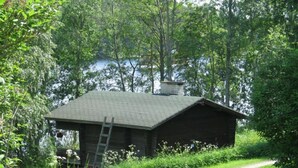 Un chalet rustique avec un toit en pente, entouré d’une végétation luxuriante et avec un lac en arrière-plan.