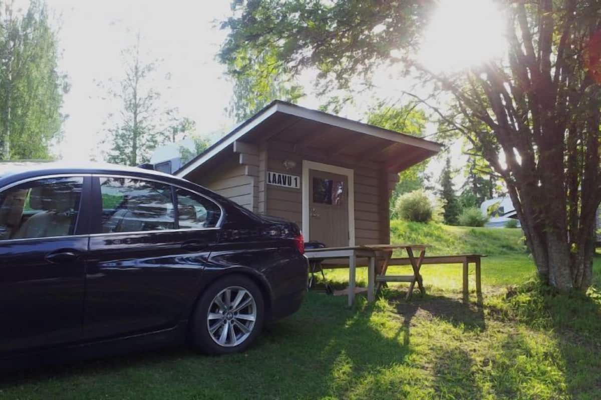A black car parked in front of a small wooden cabin with a picnic table and a bench.