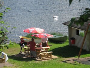 Un espace de pique-nique au bord du lac, avec des bancs et des tables en bois, un petit abri et un canoë.