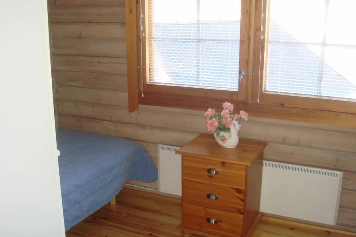 A bedroom with wooden walls, a bed, a dresser with drawers, and a radiator.