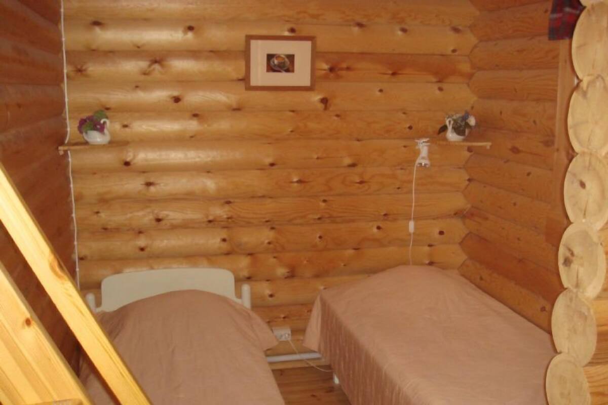 A log cabin room with two beds, a wooden wall, and a small shelf with decorative items.