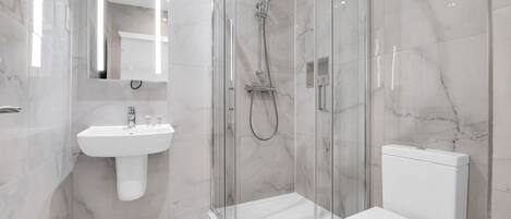 A modern bathroom with a glass-enclosed shower, a white sink, and a toilet.