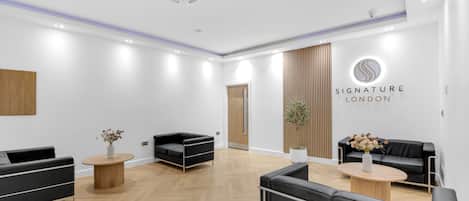 A modern reception area with black leather sofas, a wooden floor, and a sign reading 'Signature London'.
