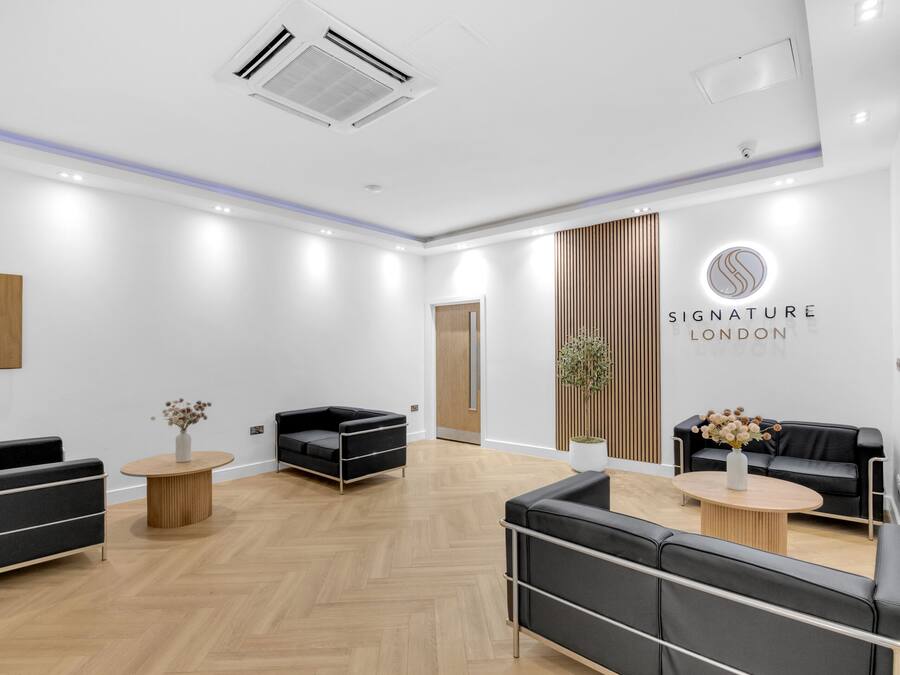 Ein moderner Empfangsbereich mit schwarzen Ledersofas, Holzboden und einem Schild mit der Aufschrift 'Signature London'.