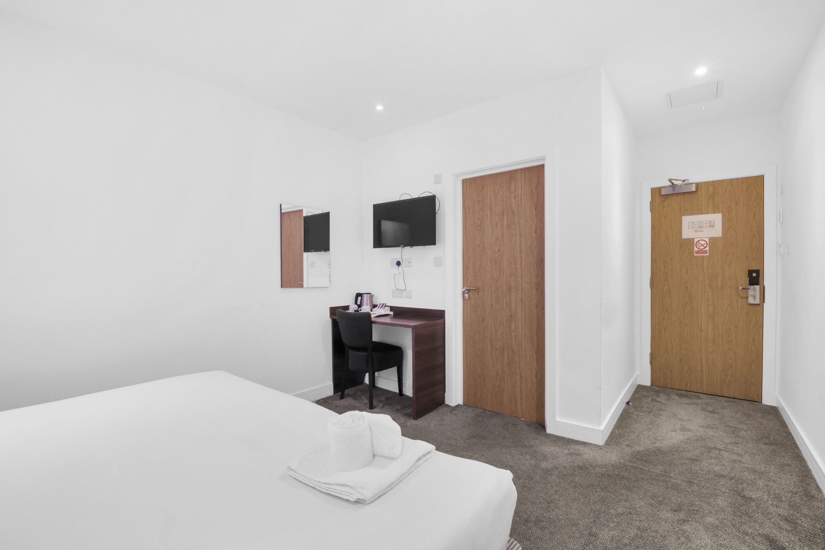 Una habitación de hotel con cama, un escritorio con silla, televisión y puerta de madera.