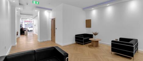 A modern reception area with a black leather sofa, a wooden floor, and a small round table with a vase of flowers.