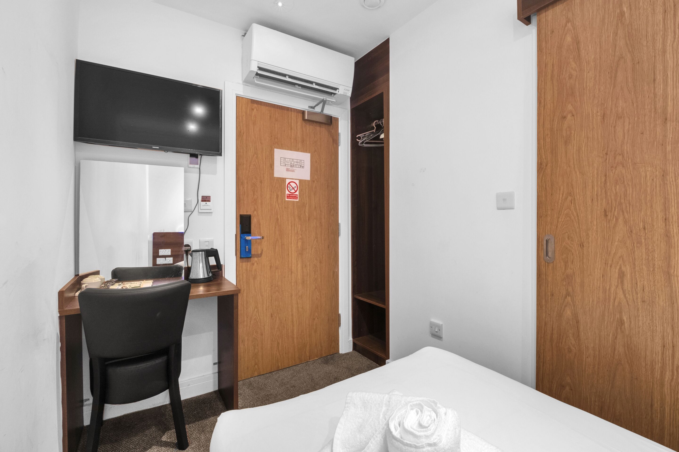 Hotelkamer met een bed, een bureau met stoel, een televisie, een airconditioner en een kledingkast.