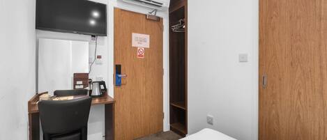 Hotelkamer met een bed, een bureau met stoel, een televisie, een airconditioner en een kledingkast.