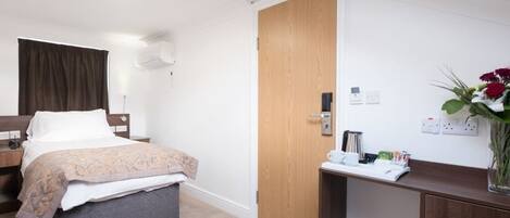 A hotel room with a bed, bedside table, desk, and a wooden door.