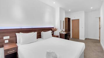 Une chambre d’hôtel moderne avec un grand lit, une tête de lit en bois, des tables de chevet, un bureau et une porte.