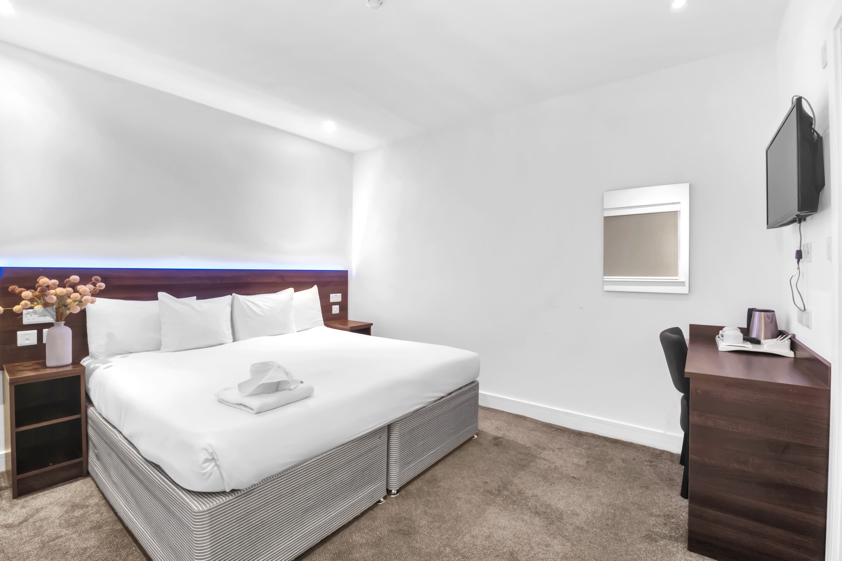 A hotel room with a large bed, a desk, a chair, a TV, and a vase with flowers.