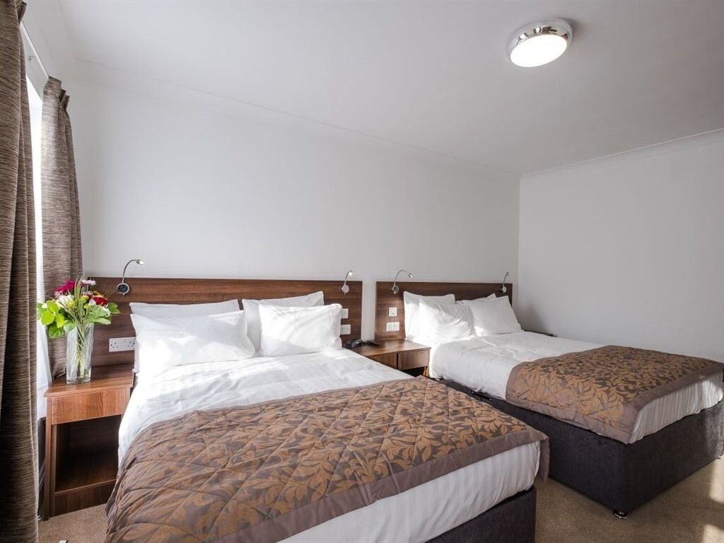 A hotel room with two beds, a nightstand with a lamp, and a vase with flowers.