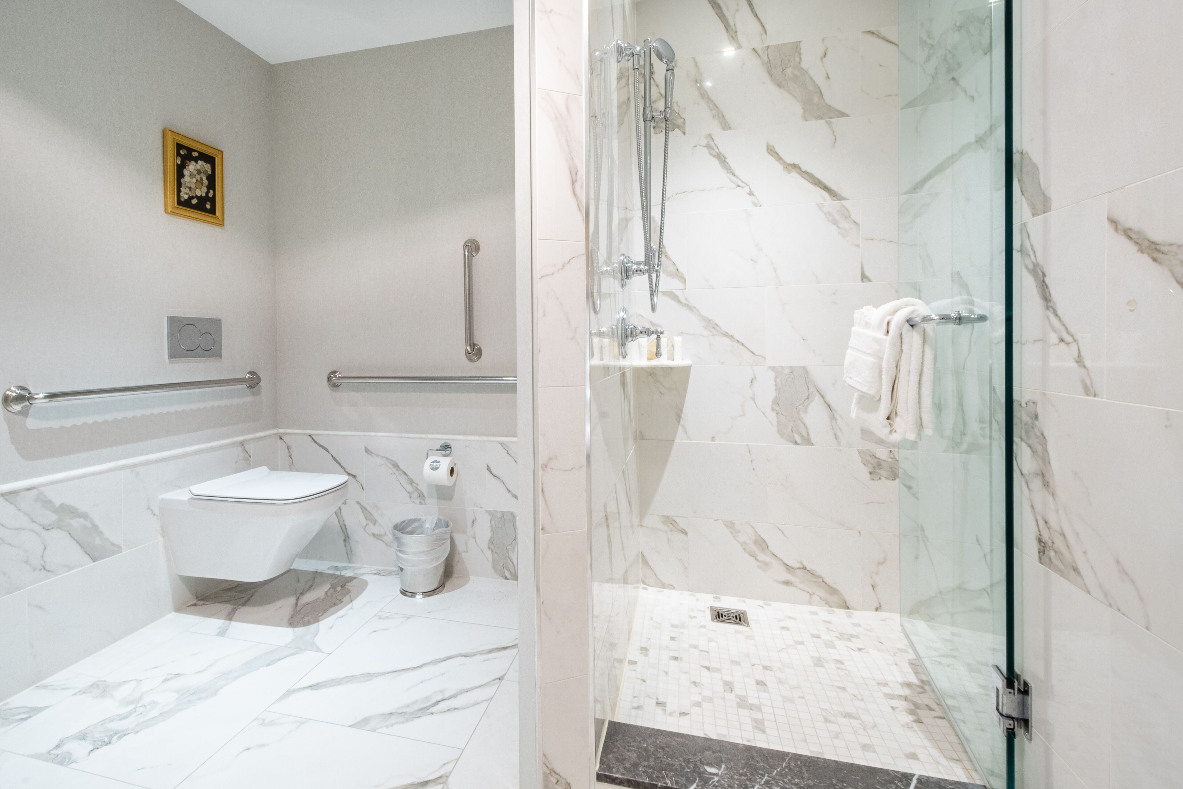 A modern bathroom with a glass-enclosed shower, a toilet, and a marble floor.
