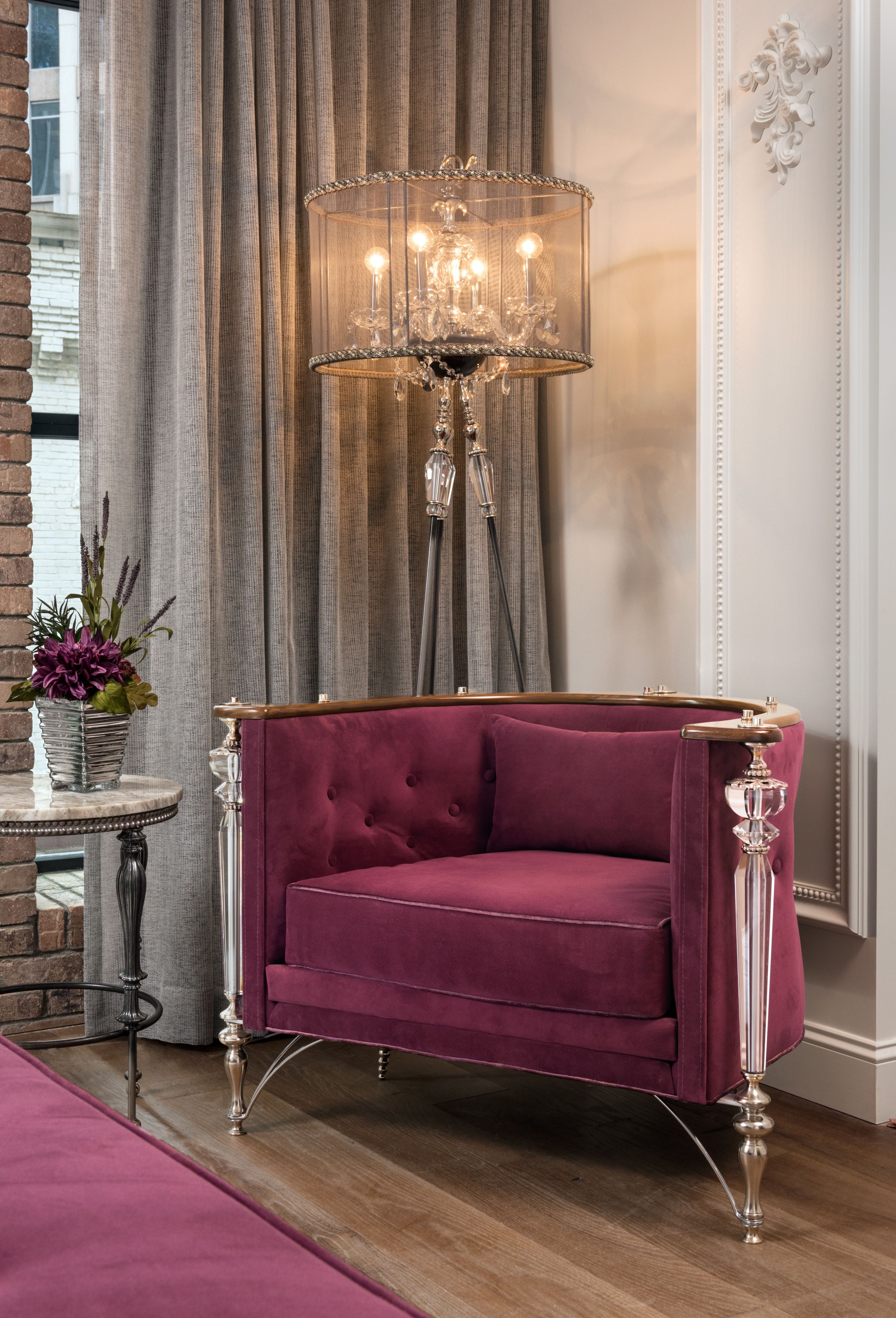 Un sofá rojo y lujoso con patas ornamentales, un candelabro de cristal y una mesita redonda con un florero.