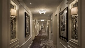 Um corredor comprido e estreito com lustres ornamentados, arandelas decorativas e um tapete estampado.