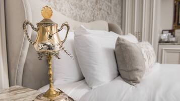 Uma cama com roupa de cama branca e um abajur decorativo prateado e dourado sobre uma superfície de mármore.