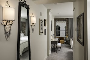A hotel hallway with a bed, a desk with a chair, and a fireplace.