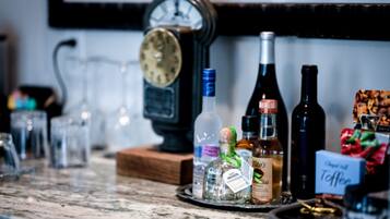 Um balcão de bar com diversas garrafas de bebidas alcoólicas, copos e um relógio.