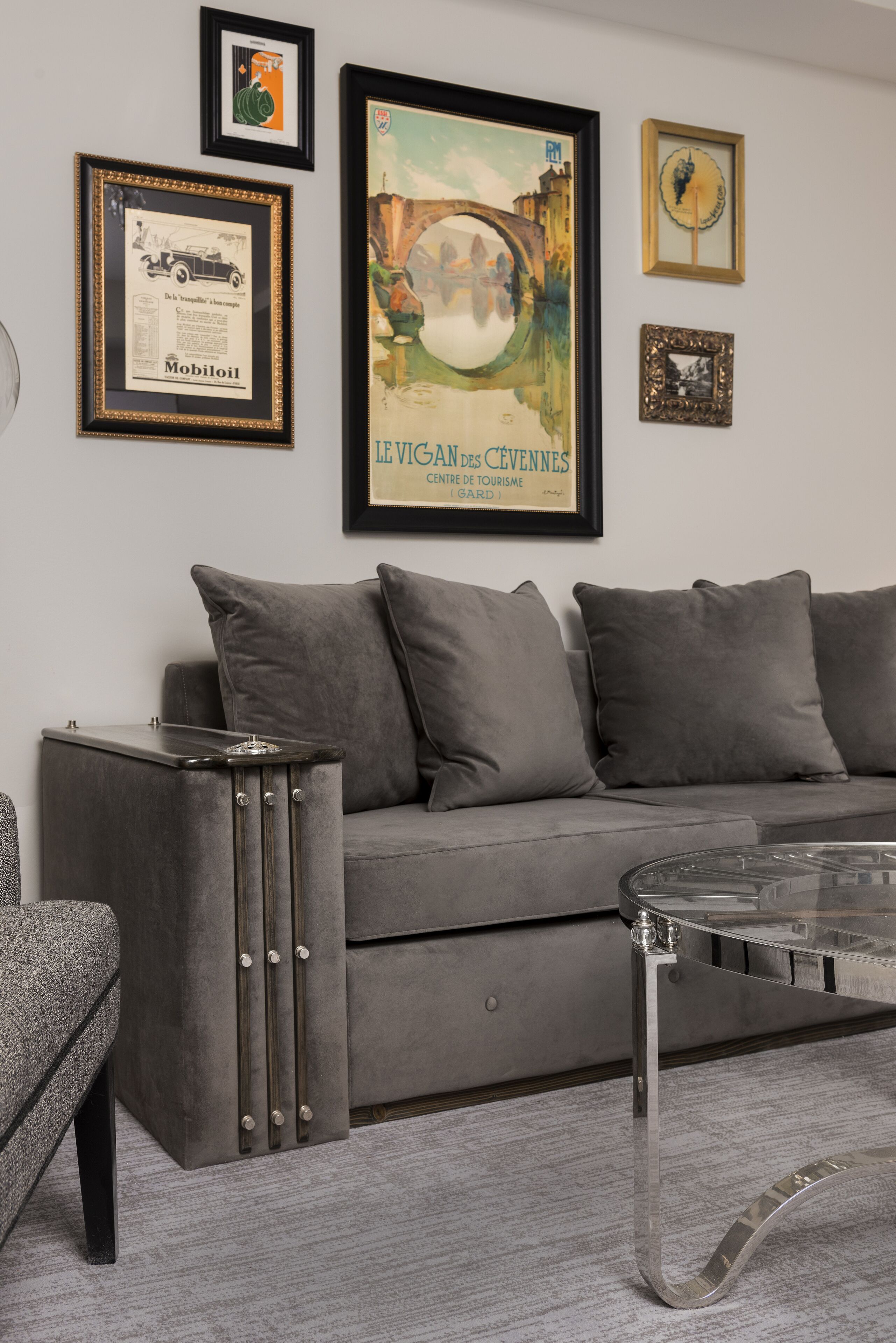 Ein modernes Wohnzimmer mit einem grauen Sofa, einem Glastisch und gerahmten Kunstwerken an der Wand.