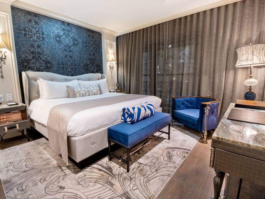 A hotel room with a large bed, a blue armchair, a marble side table, and a wall with a textured pattern.
