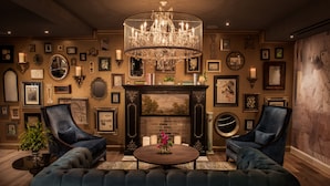 Uma sala de estar luxuosa com um lustre imponente, lareira e uma coleção de obras de arte emolduradas nas paredes.