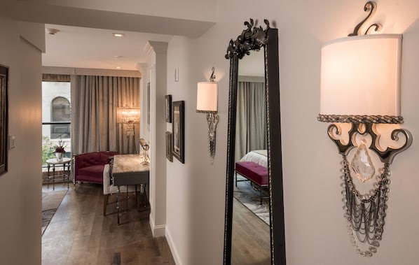 A hotel room with a large mirror, a bedside table, a red sofa, and a view of the outside. - The Ivey's Hotel (Charlotte)