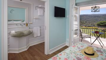 A bedroom with a stone sink, a flat-screen TV, and a balcony with a view of the hills.