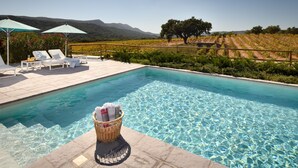 A pool with clear water, surrounded by lounge chairs and umbrellas, with a vineyard and hills in the background. - Hotel Casa Palmela (Setubal)
