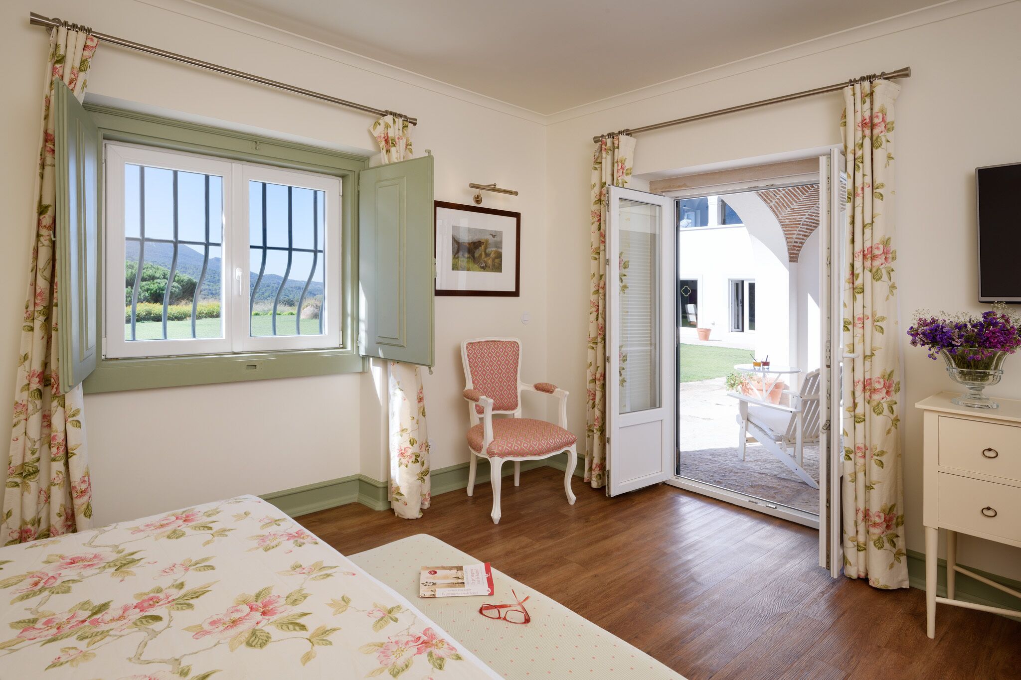 A room with a bed, a chair, a desk, and a door leading to an outdoor area.