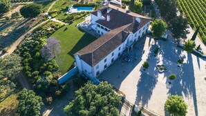 An aerial view of a large estate with a central building surrounded by expansive vineyards, a swimming pool, and a paved courtyard. - Hotel Casa Palmela (Setubal)