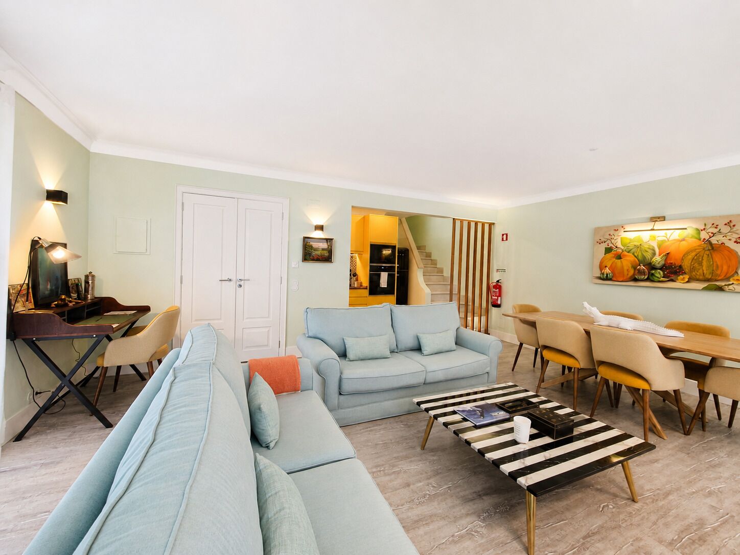 A living room with a sofa, a dining table with chairs, a coffee table, and a painting on the wall.