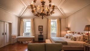 A room with a large bed, a sitting area, a bathtub, and a chandelier. - Hotel Casa Palmela (Setubal)